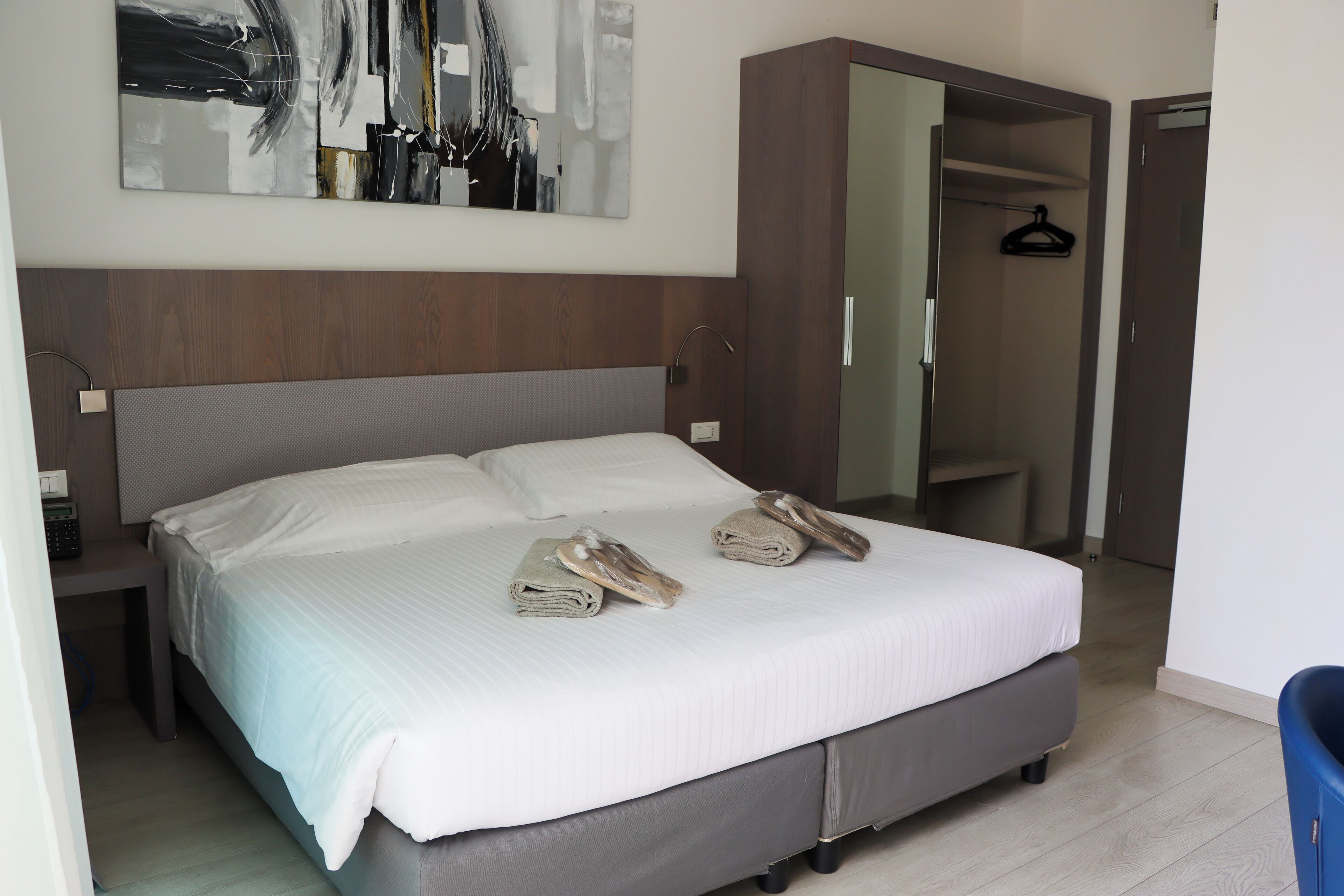 Una cama bien hecha con toallas y pantuflas, un cabecero de madera, un espejo grande y un armario.