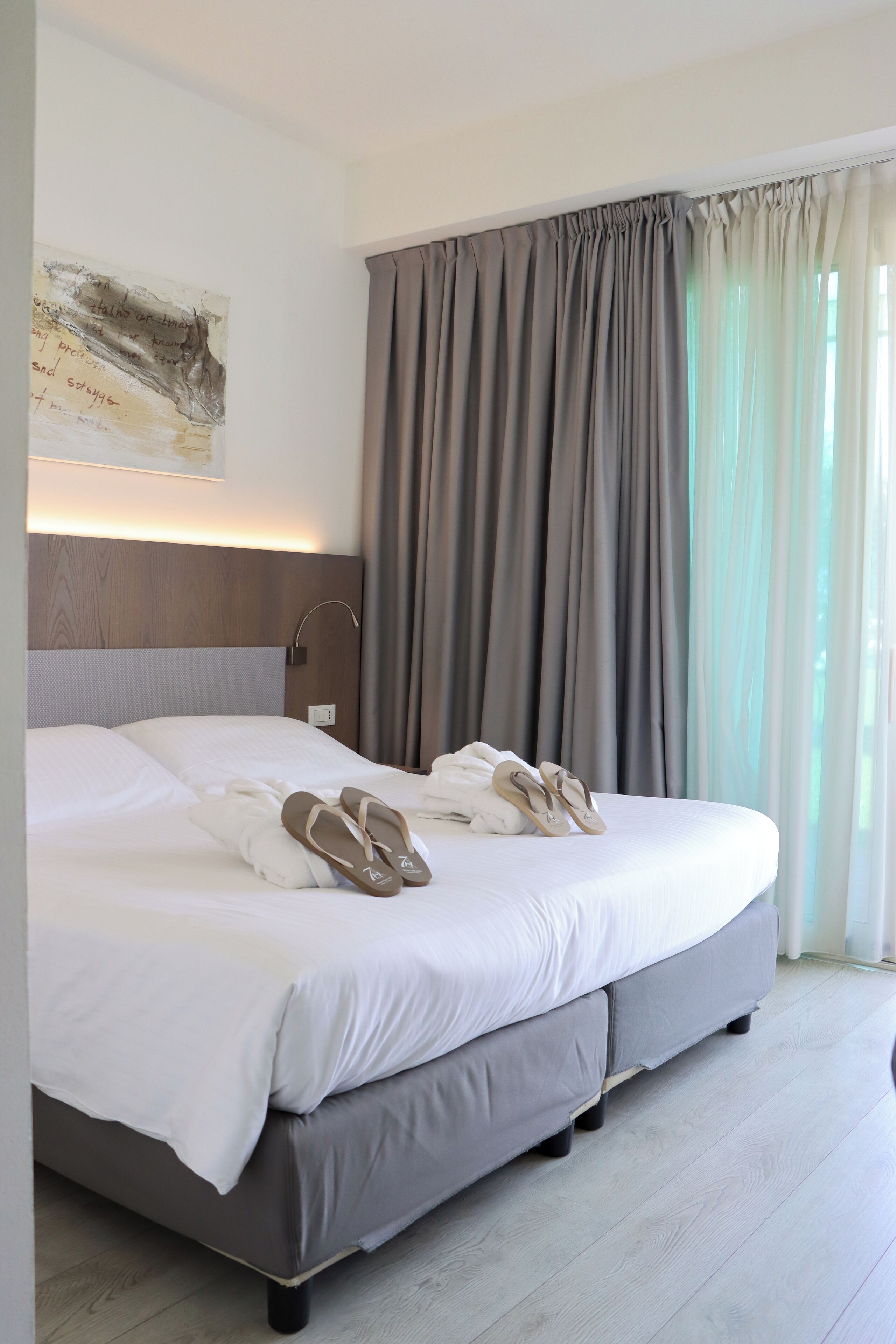 A modern hotel room with a large bed, grey curtains, and a wall-mounted artwork.