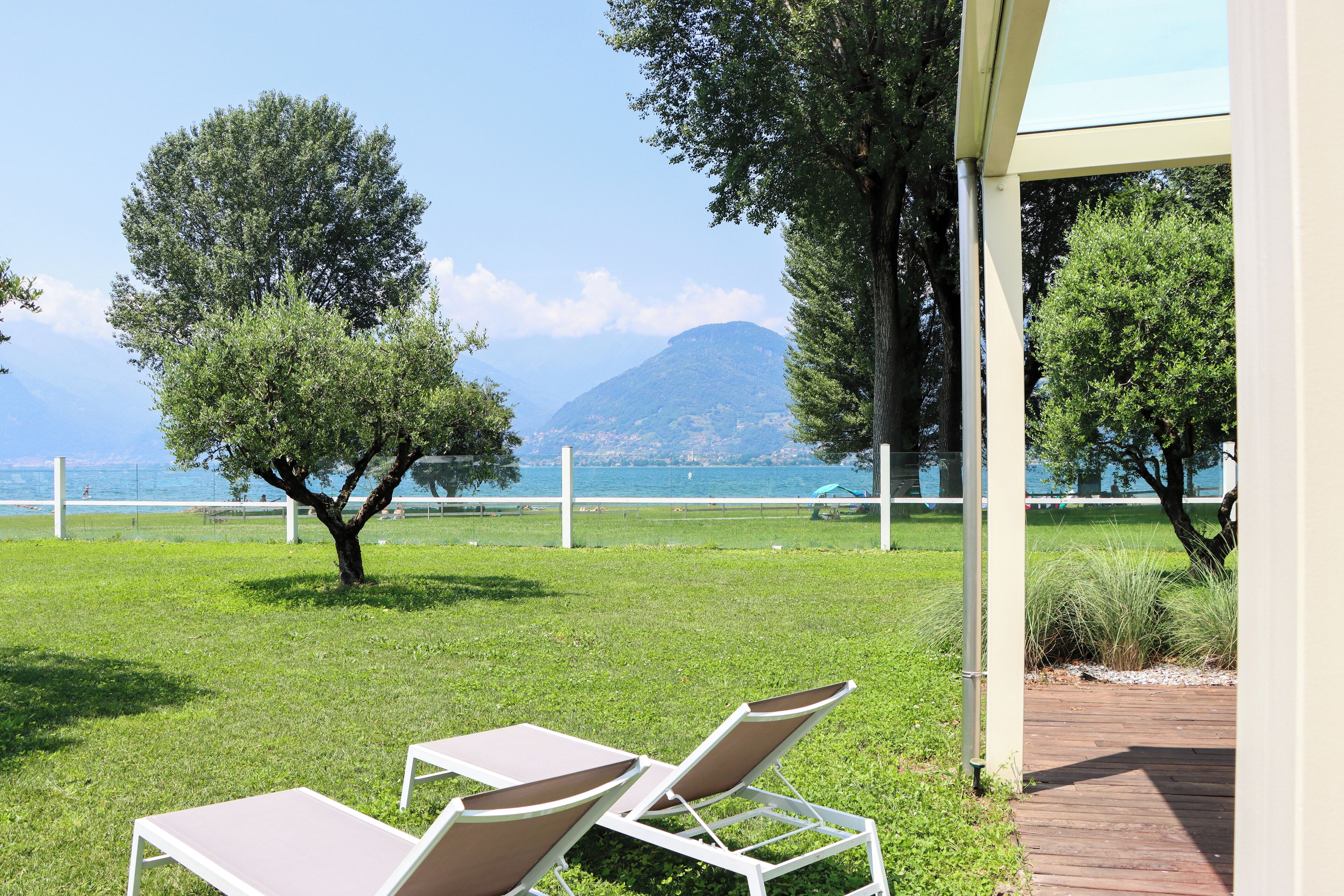 A grassy outdoor area with two white lounge chairs and a wooden deck.