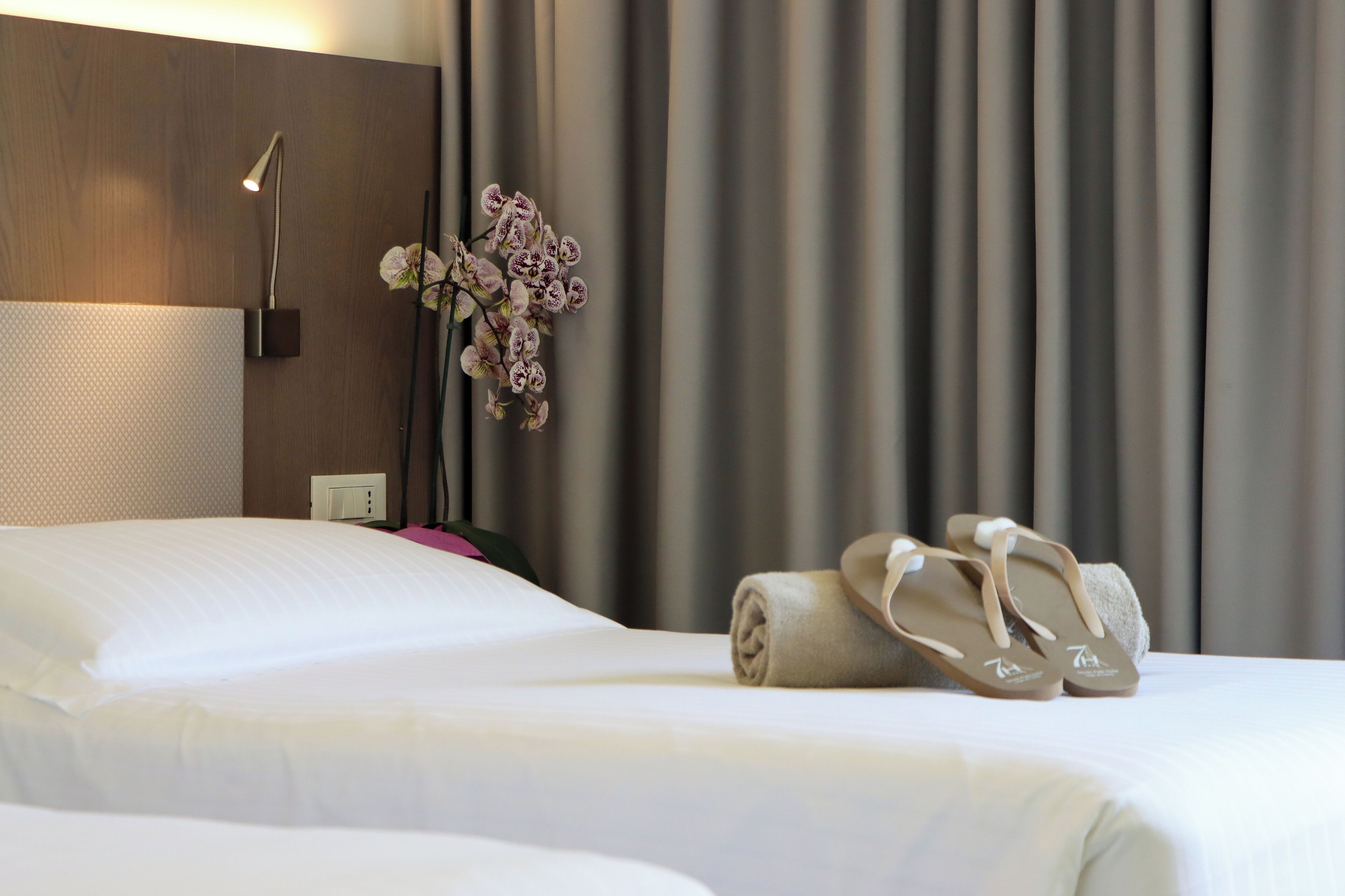 Een hotelkamer met een net opgemaakt bed, een paar slippers, een lamp en een decoratieve orchidee.