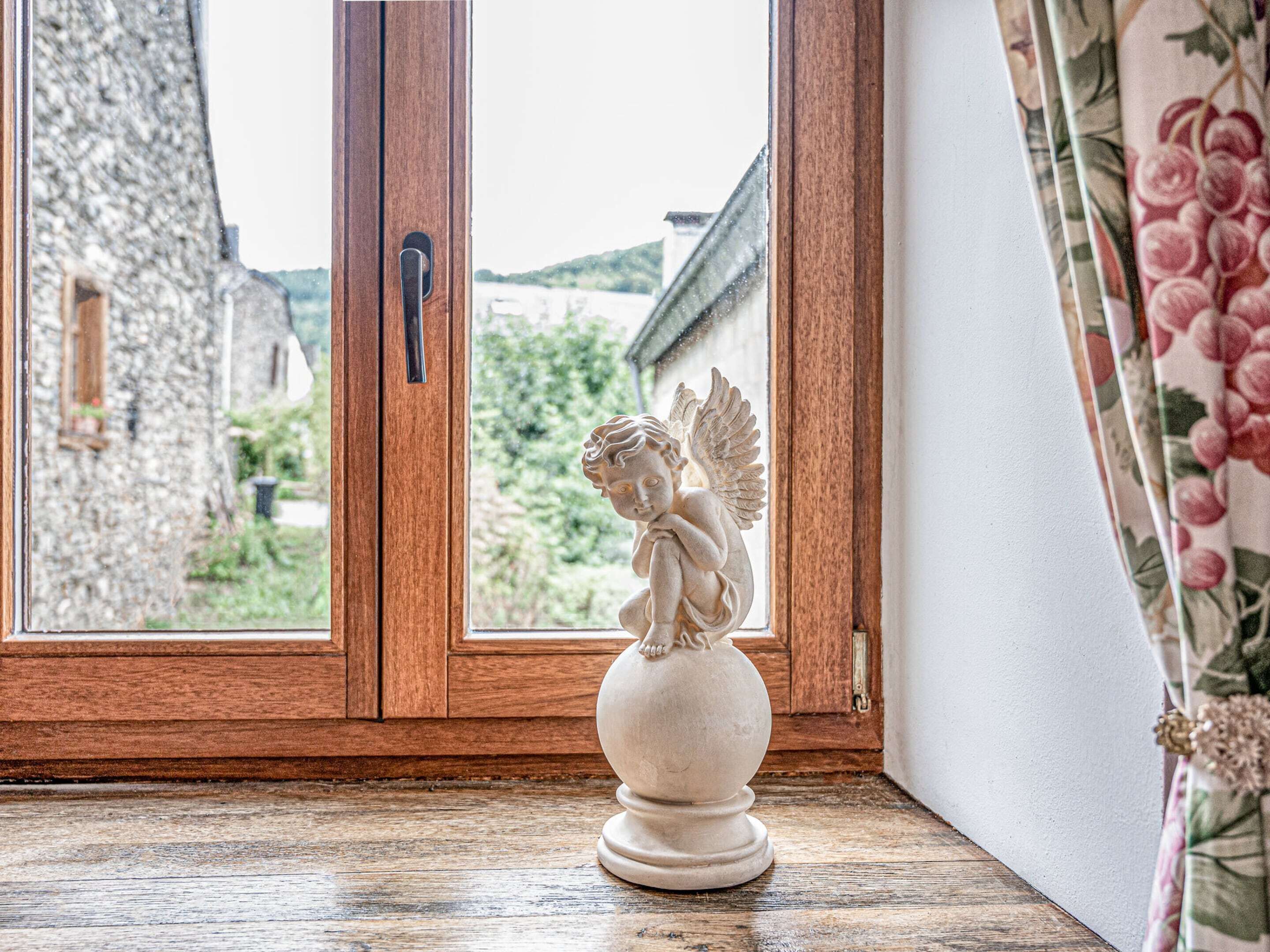 A room with a wooden floor, a stone wall, and a window with a view of greenery and a building outside.