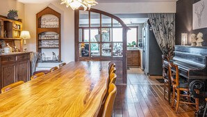 Un comedor con mesa y sillas de madera, una araña y vistas por un gran ventanal.