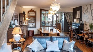 Una sala acogedora con un sofá de cuero, una mesa de comedor y una zona de cocina con un piano.
