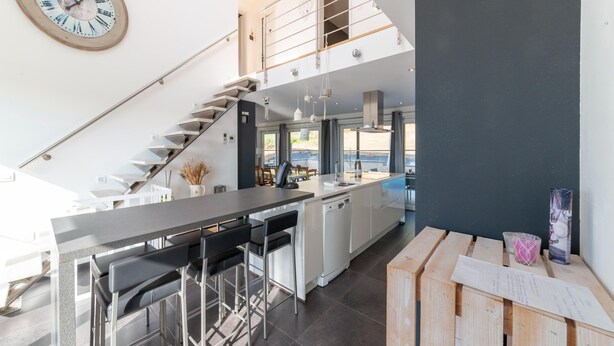 Een moderne keuken met een centraal eiland, barkrukken, een trap en uitzicht op de omgeving.
