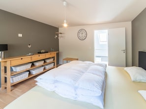 Une chambre à coucher avec un lit, une commode en bois avec des paniers, une horloge murale et une porte donnant sur un balcon.