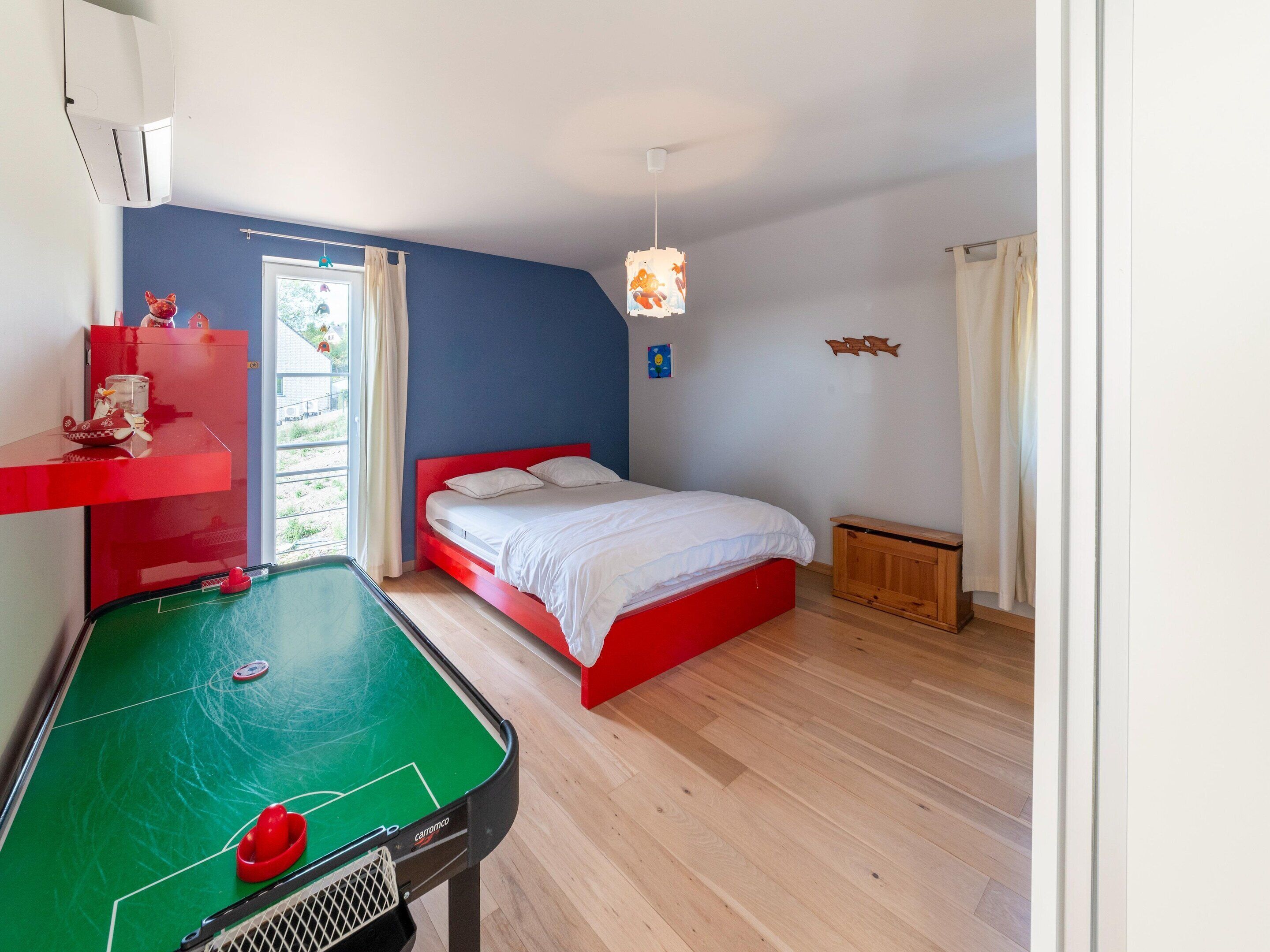 Una habitación con mesa de billar, cama con cabecera roja y ventana con cortinas.