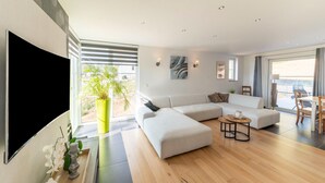 Een moderne woonkamer met een hoekbank, een flatscreen-tv, een eethoek met een tafel en stoelen, en een groot raam met uitzicht.