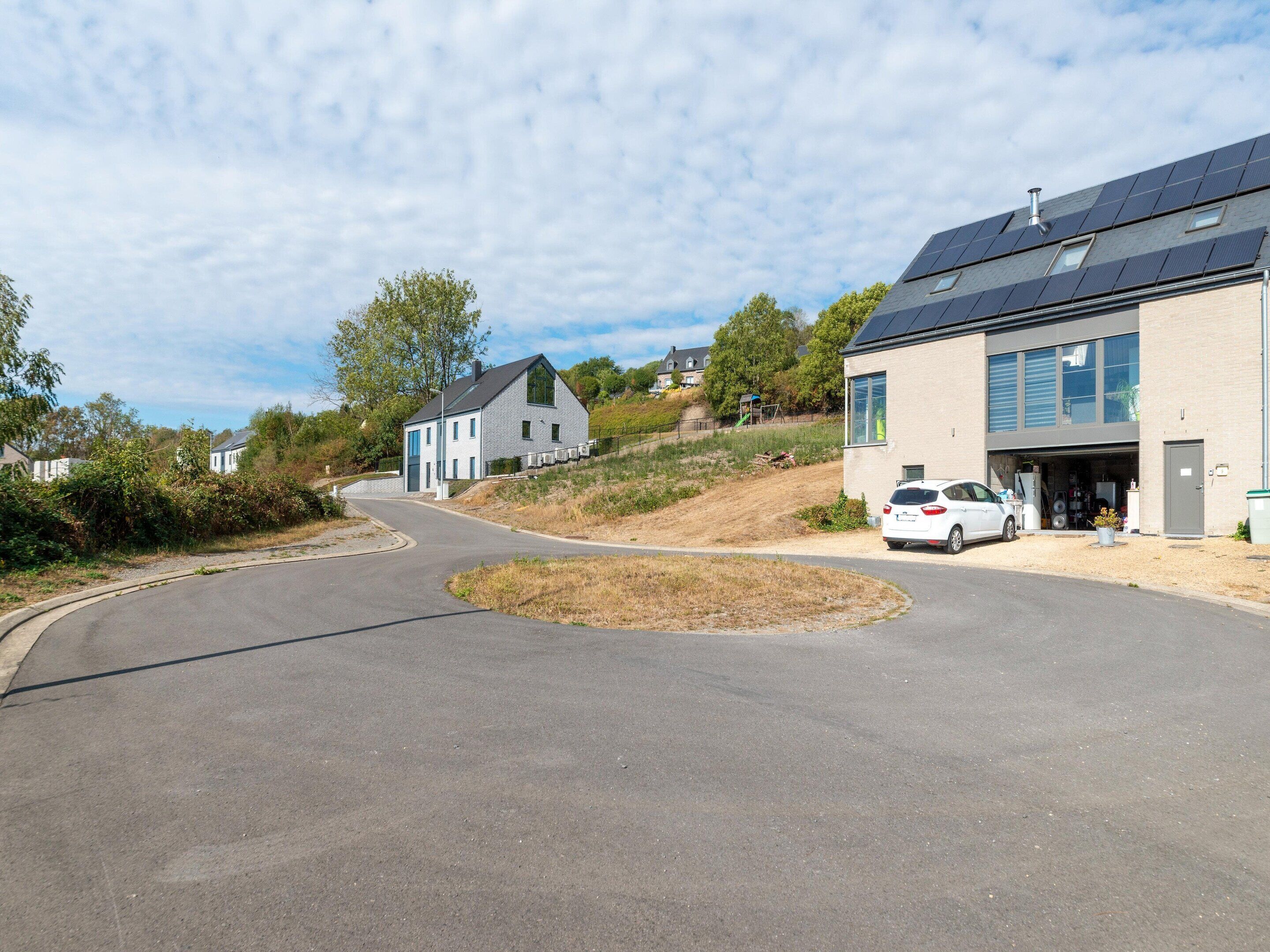 A residential area with modern houses, a curved road, and a parked car in front of a building with solar panels.
