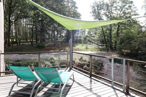 A deck with two green chairs and a green canopy, overlooking a forested area.