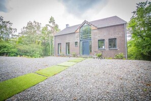 A two-story brick house with a modern design, a gravel driveway, and a small garden area.
