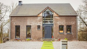 A brick house with a dark blue door, a large window, and a gravel driveway.