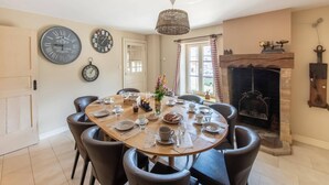 A dining room with a round table set for six, surrounded by chairs. There are three wall clocks, a fireplace with a mantel, and a window with curtains. - Welcoming Holiday Home in Vresse-sur-semois With Terrace (Vresse-sur-Semois)