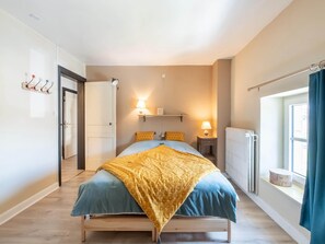 Un dormitorio con cama, lámparas de noche, una ventana con cortinas, un radiador y una puerta.