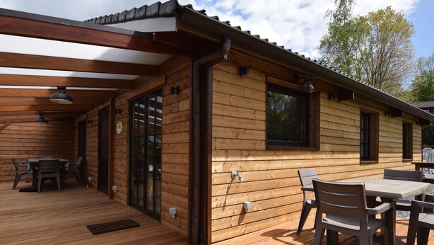 A wooden cabin with a deck, outdoor seating, and a covered area.