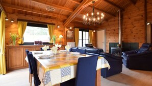 A wooden cabin interior with a dining area, a sofa, and a fireplace.