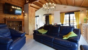 A cozy living room with a large blue leather sofa, a television mounted on the wall, and a wooden ceiling with exposed beams.
