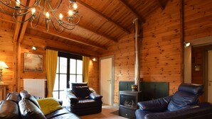 A cozy log cabin interior with leather sofas, a fireplace, and a chandelier.