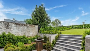 A stone staircase leading up to a patio area with a fire pit and a view of a green lawn and trees. - Spacious Family Holiday Home (Mont-de-l'Enclus)