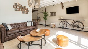 A modern living room with a brown leather sofa, wooden coffee table, and ottomans, a hanging light fixture, a bicycle, and a TV mounted on the wall. - Spacious Family Holiday Home (Mont-de-l'Enclus)