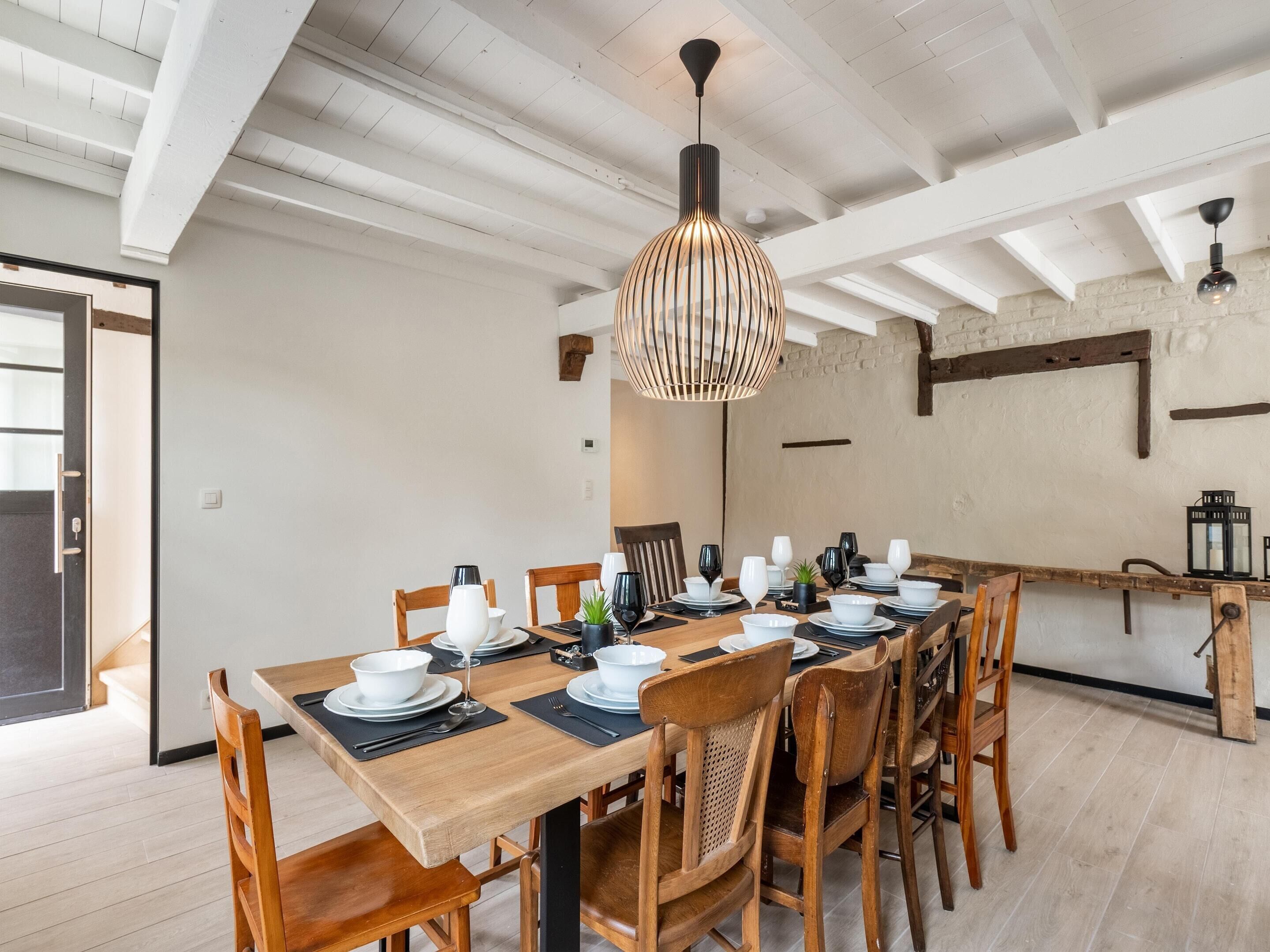 A dining area with a long wooden table set for six, surrounded by wooden chairs.