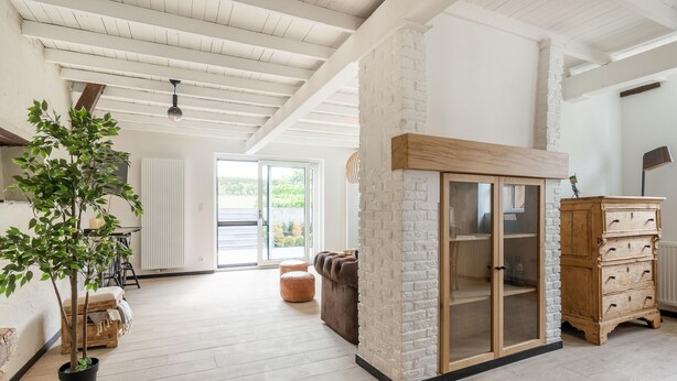 A spacious living room with a wooden floor, a white brick accent wall, a wooden cabinet with drawers, and a large sliding glass door leading to a balcony. - Spacious Family Holiday Home (Mont-de-l'Enclus)