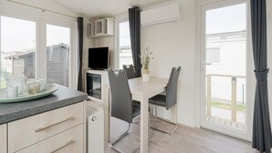 A modern kitchen with a dining area, a built-in TV, and a balcony with curtains. - Middelkerke Mobile Home With Garden (Middelkerke)
