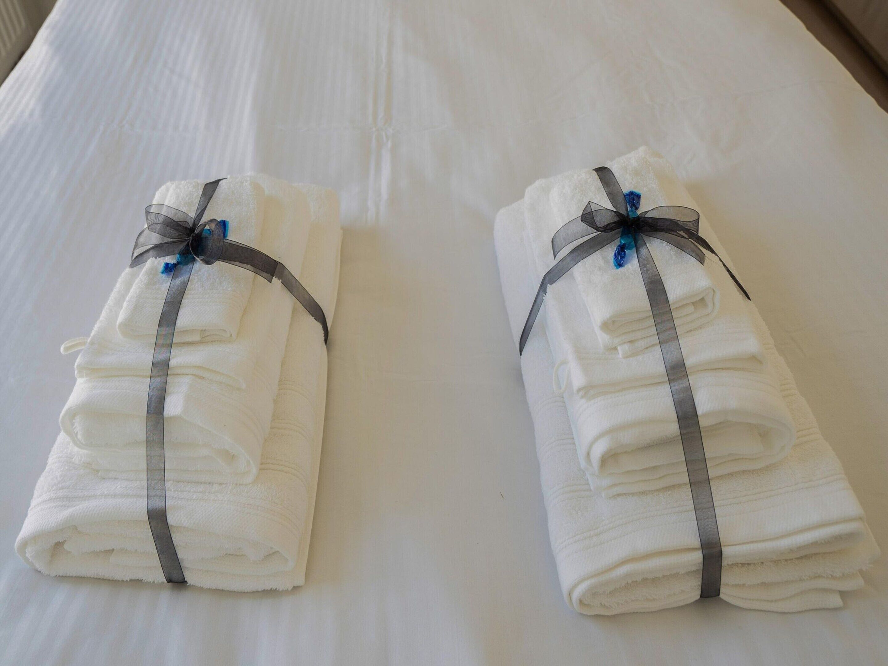 Two neatly folded white towels with gray ribbons and blue accents, placed on a white bed.