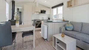 A modern kitchen with a central island, a dining area with a table and chairs, and a grey sofa in a living area. - Middelkerke Mobile Home With Garden (Middelkerke)