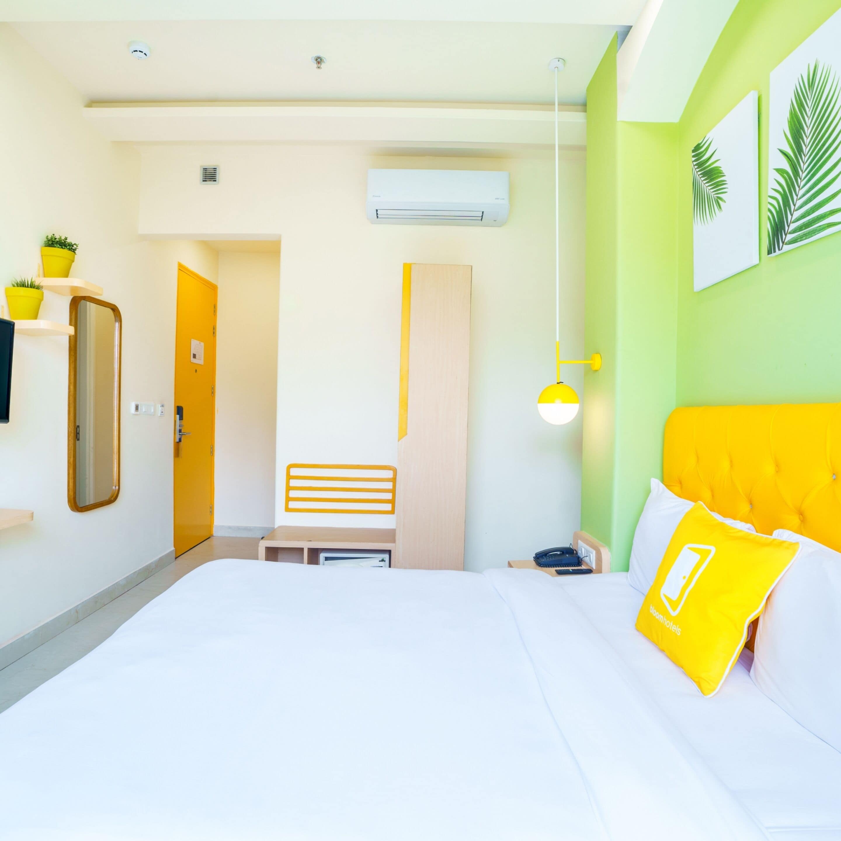 Une chambre d’hôtel comprenant un lit, une table de chevet, un miroir, une armoire, un bureau et une lampe suspendue.