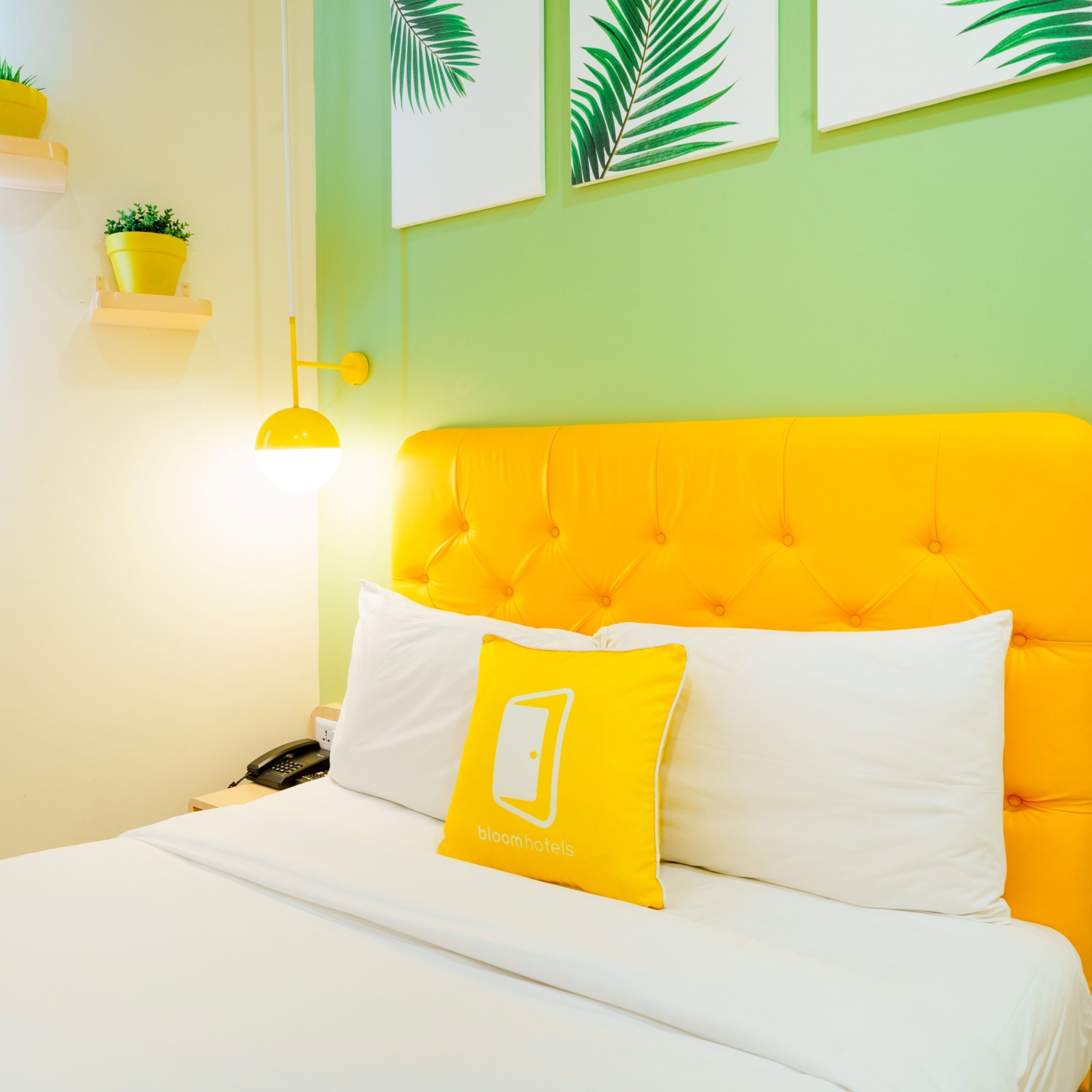 Un letto con testiera gialla e biancheria da letto bianca, un cuscino giallo con un logo e una lampada da comodino.