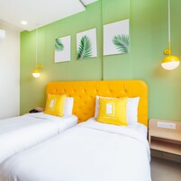 Una habitación de hotel con un cabecero amarillo brillante, dos camas con ropa blanca y tres piezas de arte mural con hojas de palma.