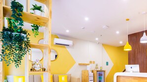 A modern hotel lobby with a wooden reception desk, a sofa, a coffee table, and a bookshelf with plants and books. - Bloom Hotel - Heritage Walk (Amritsar)