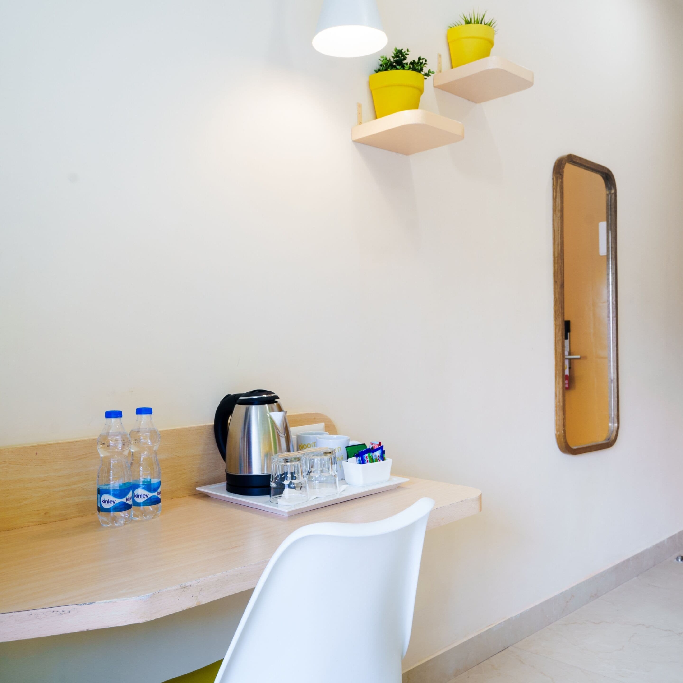 Ett hotellrum med ett skrivbord i trä, en vit stol, en spegel, ett bricka med en vattenkokare, vattenflaskor, glas och en skål med snacks.