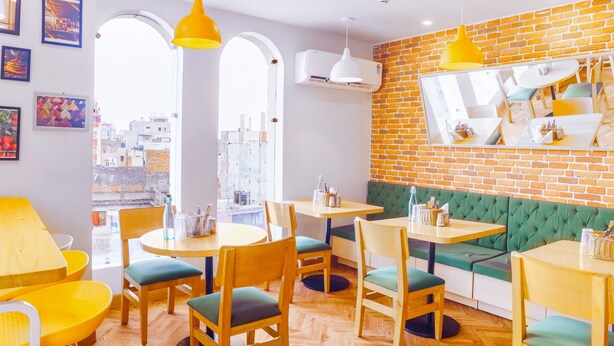 A restaurant interior with wooden tables, green cushioned booths, and yellow pendant lighting. - Bloom Hotel - Heritage Walk (Amritsar)