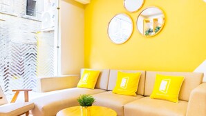 A modern living room with a yellow sofa, a round coffee table with a plant, and a bright yellow accent wall. - Bloom Hotel - Heritage Walk (Amritsar)