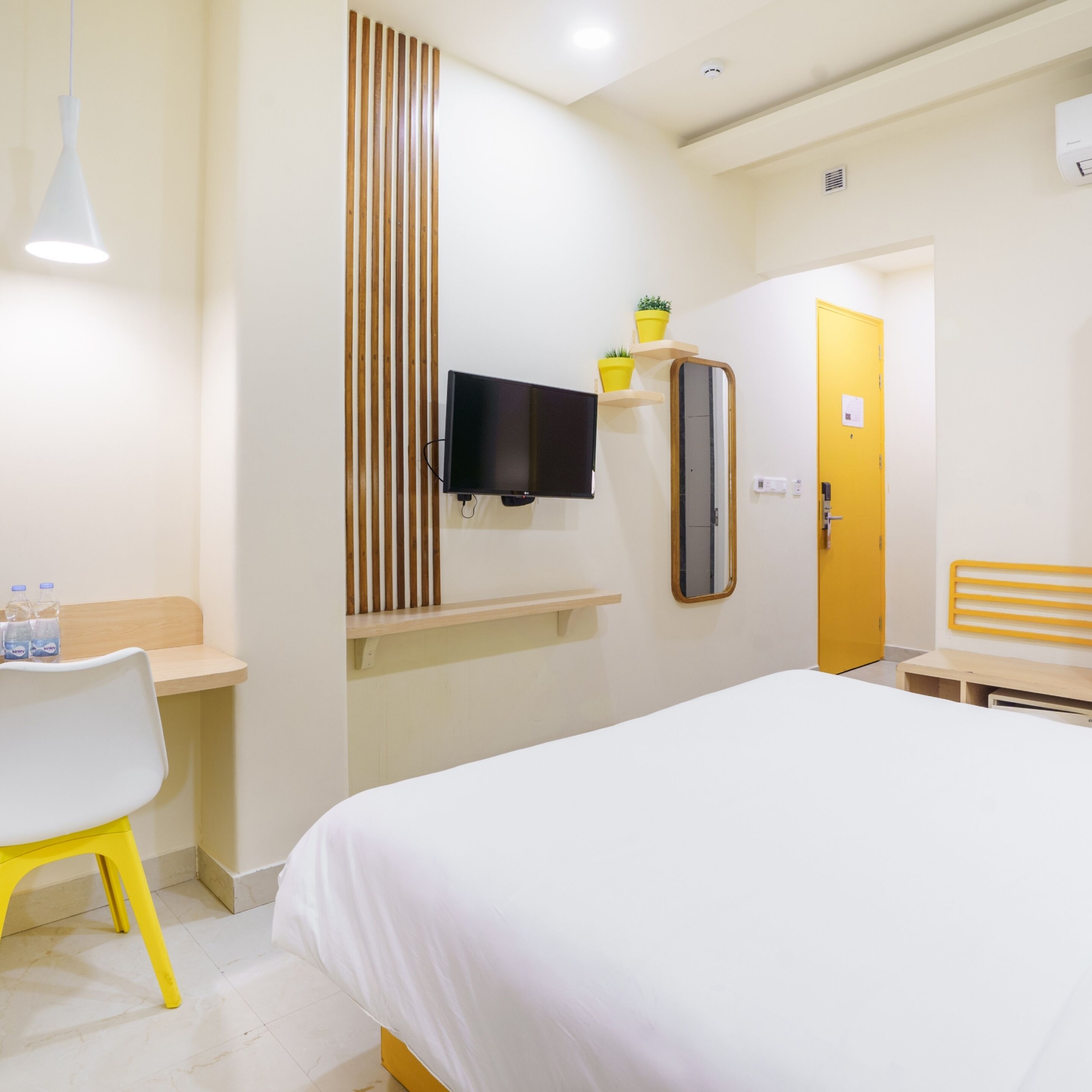 A hotel room with a bed, a desk with a chair, a television, a mirror, and a door.