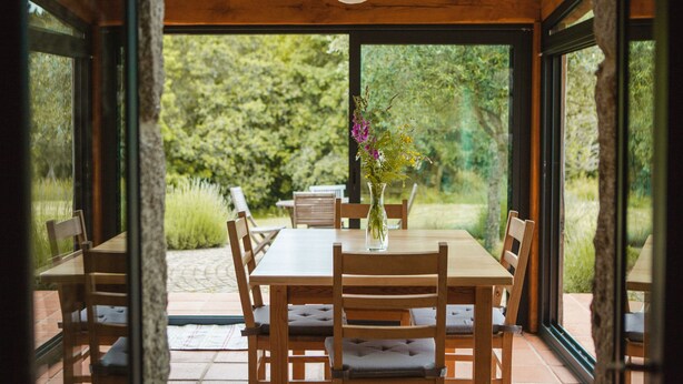 A wooden dining table with chairs, a vase with flowers, and a view of greenery outside. - One of two private and intimate casitas. Surrounded by nature. (Moraña)