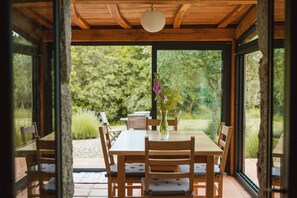 Una mesa de madera con sillas, un jarrón con flores y vistas a zonas verdes al exterior.