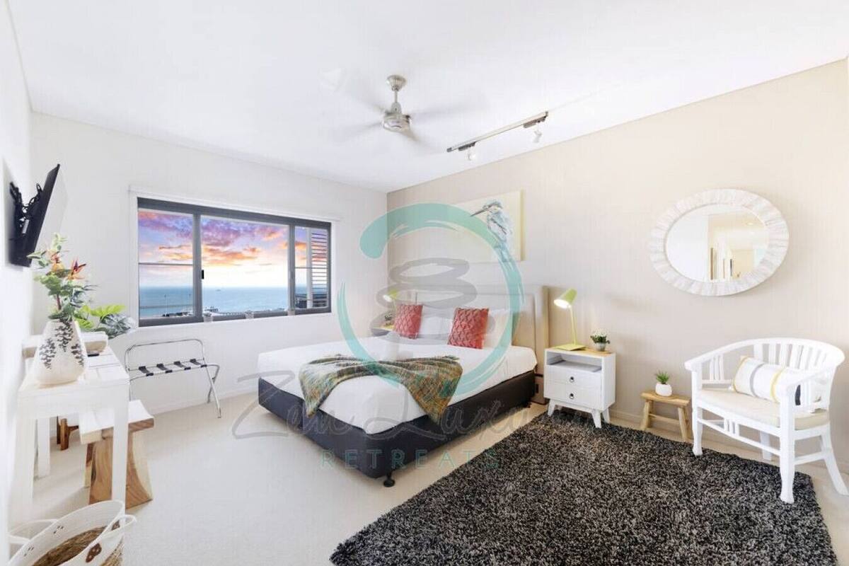 Un dormitorio moderno con cama, mesitas de noche, una silla, un ventanal con vistas y un ventilador de techo.