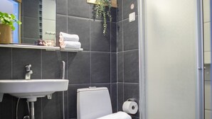 A modern bathroom with a white toilet, a sink, and a shower area. - Hotelli Uusikuu (Mikkeli)