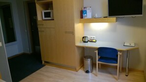 A compact kitchenette with a microwave, coffee maker, and small trash bin. - Hotelli Uusikuu (Mikkeli)