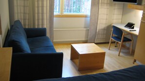 A room with a blue sofa, a wooden coffee table, a desk with a chair, and a television mounted on the wall. - Hotelli Uusikuu (Mikkeli)