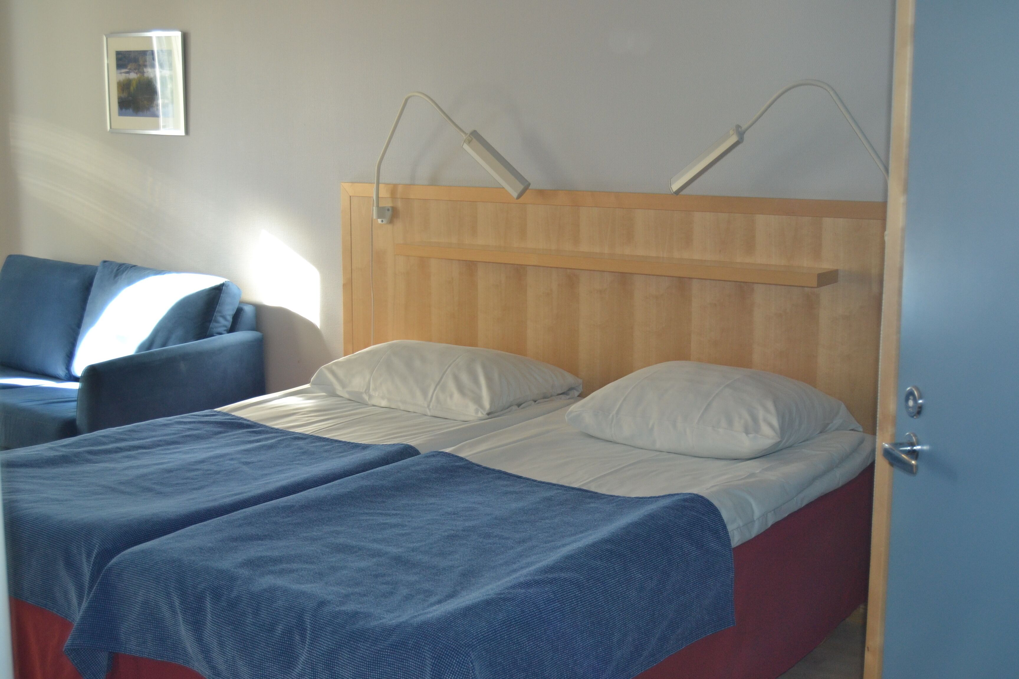 A room with two beds, a wooden headboard, and a blue door.