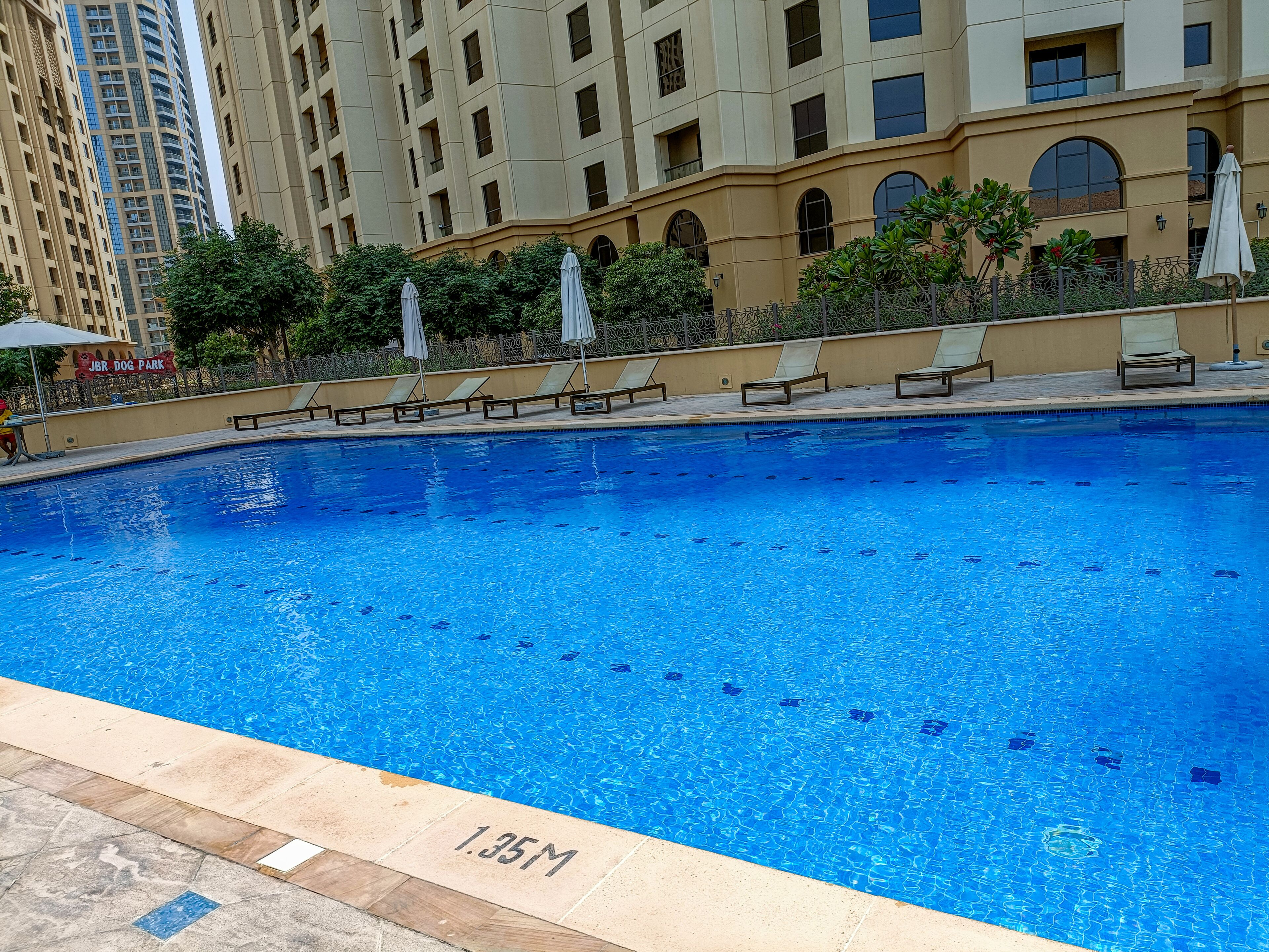A swimming pool with lounge chairs and umbrellas, surrounded by high-rise buildings.
