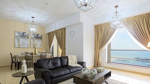 A modern living room with a black leather sofa, a dining area with a table and chairs, and a large window offering a view of the sea. - Marco Polo - Full Sea & Dubai Eye View | 2 BR | Near JBR Beach (Dubai)