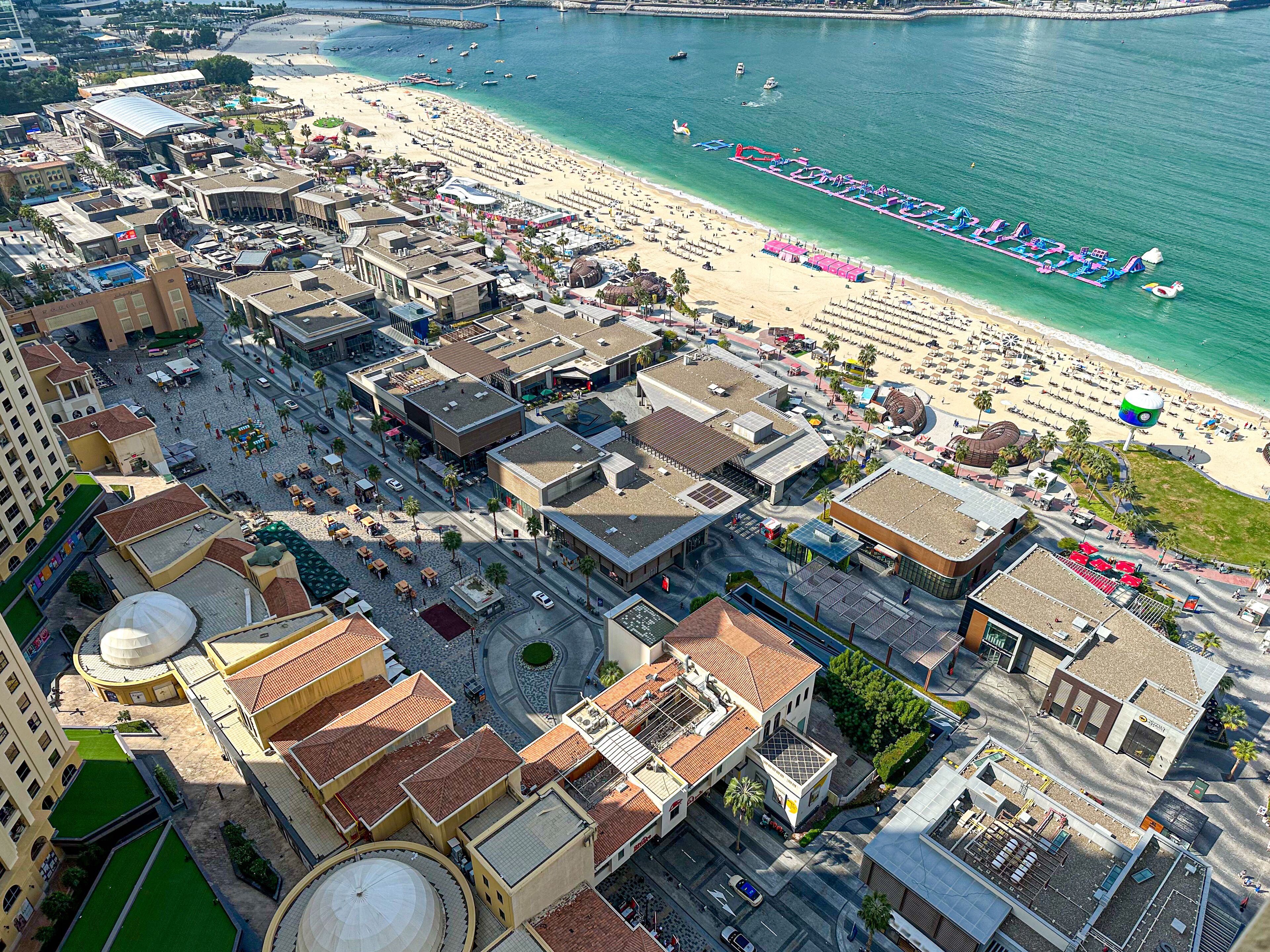 Vue aérienne d’une ville côtière avec une plage, des bâtiments et un port de plaisance.