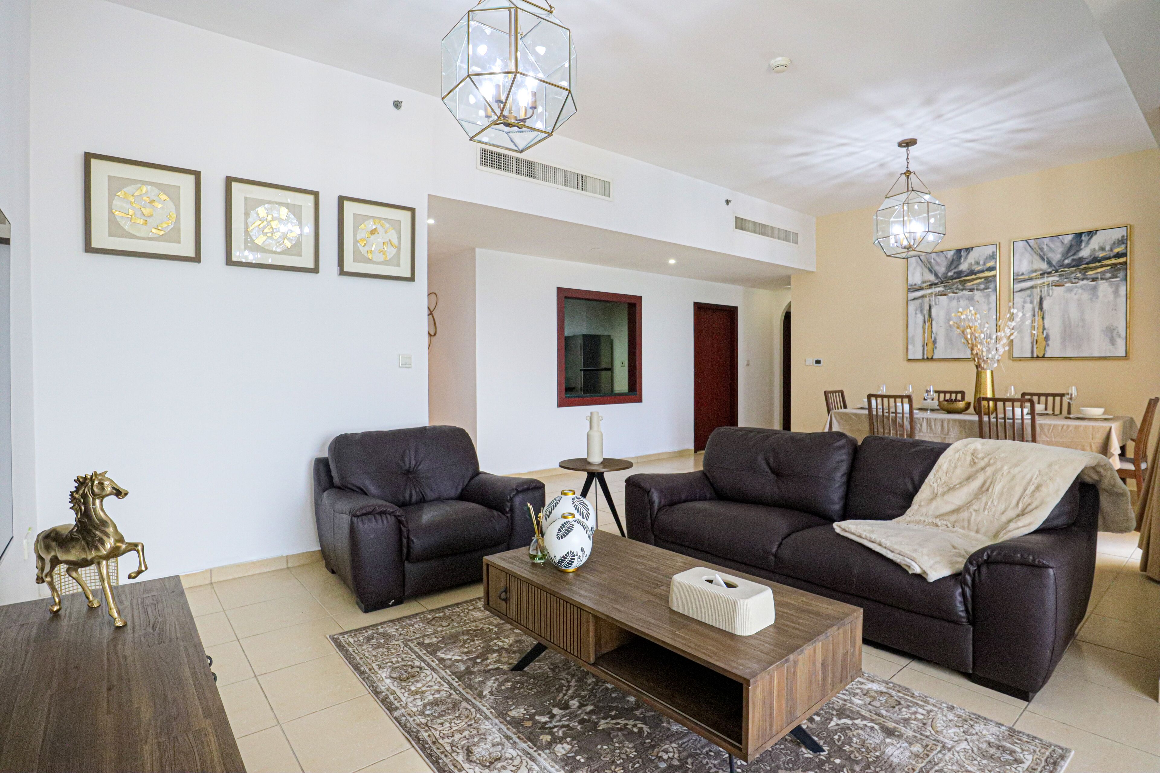 A modern living room with a sofa, coffee table, and decorative items. There are framed pictures on the wall and a chandelier.