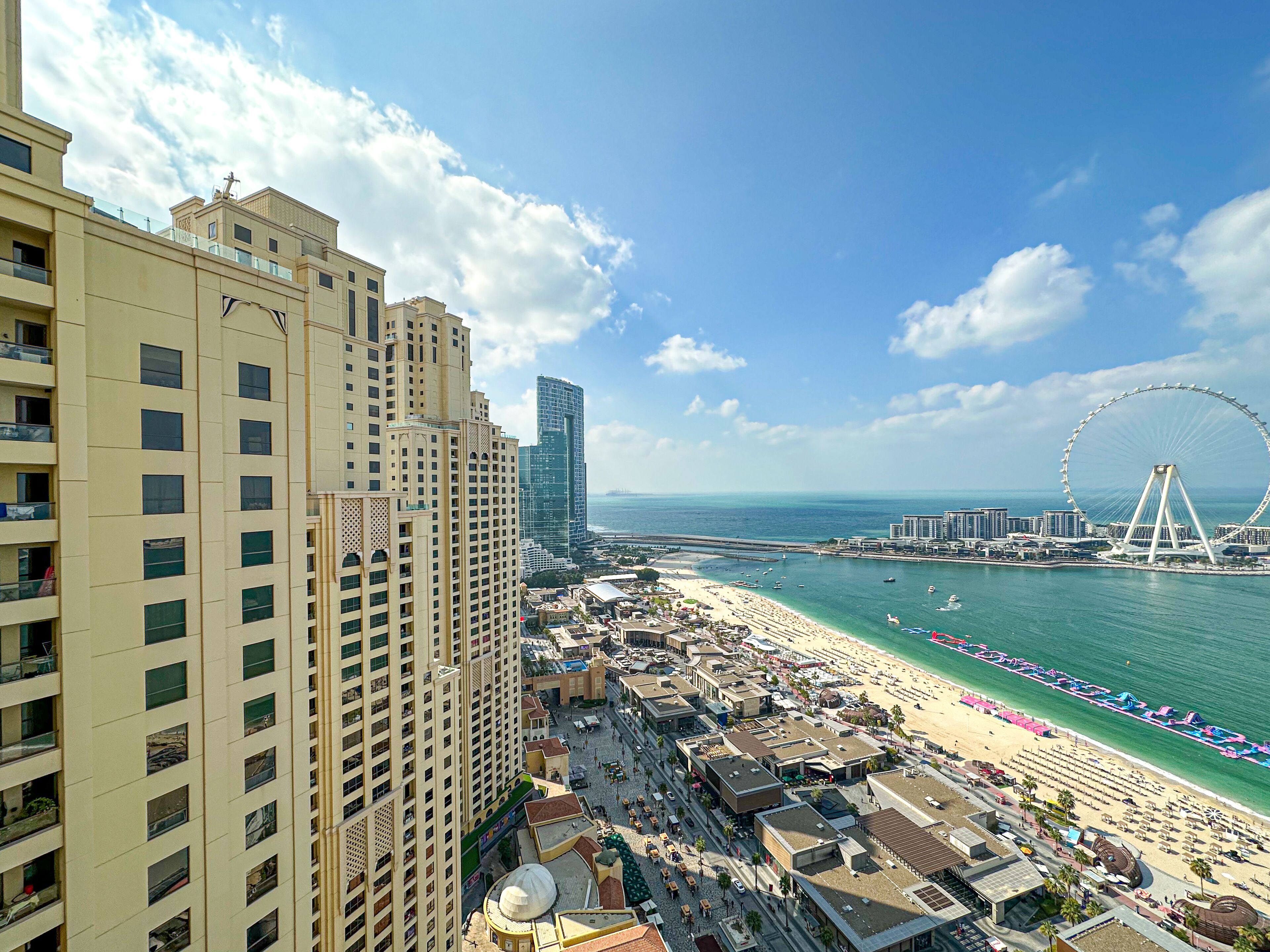 A coastal cityscape with high-rise buildings, a beach, and a large Ferris wheel.