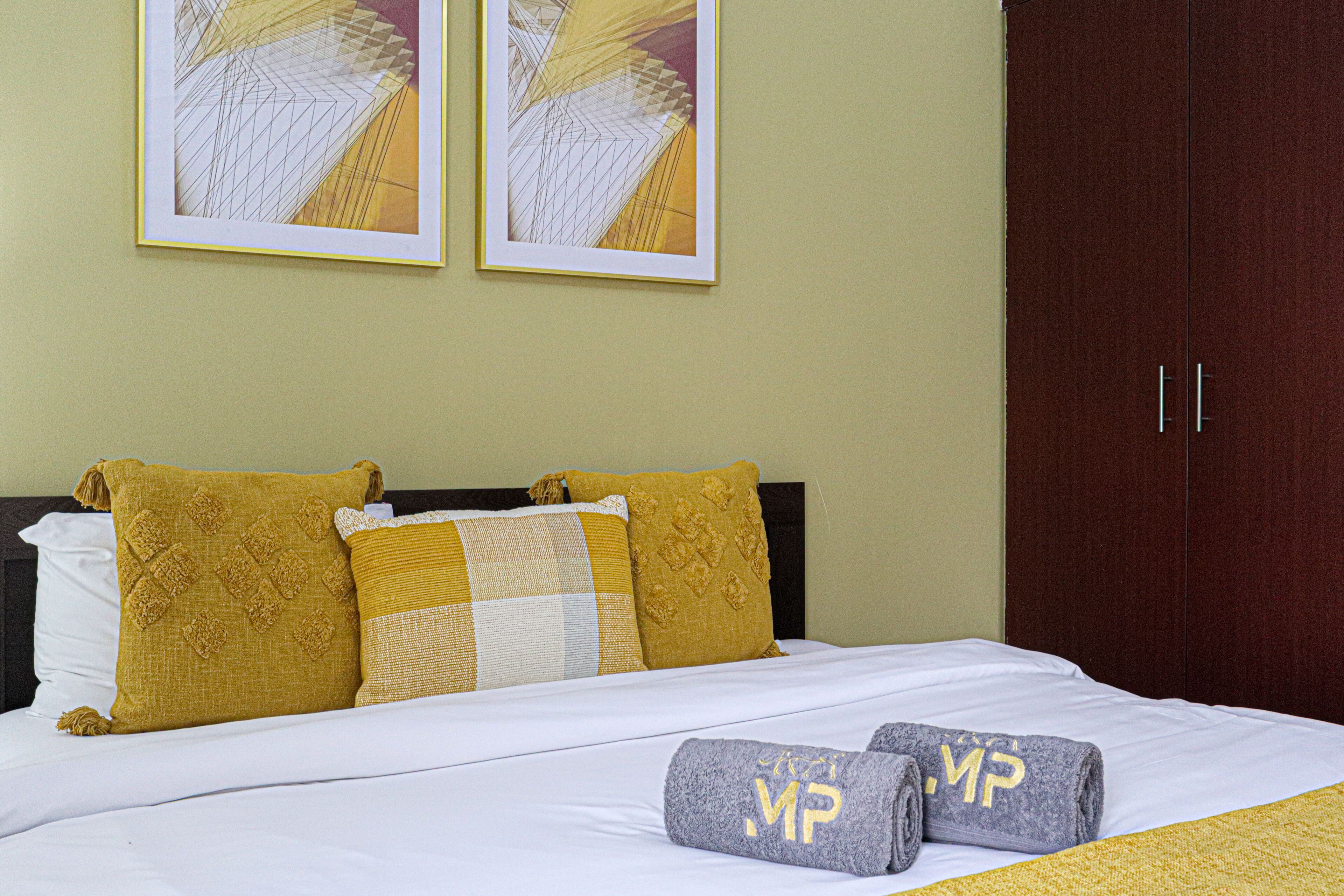 A hotel room with a bed, pillows, a wardrobe, and two framed pictures on the wall.