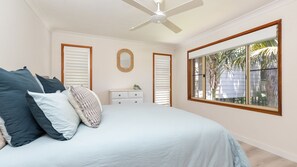 Relax in this serene bedroom with a large bed, ceiling fan, and a window offering a view of the outdoors.